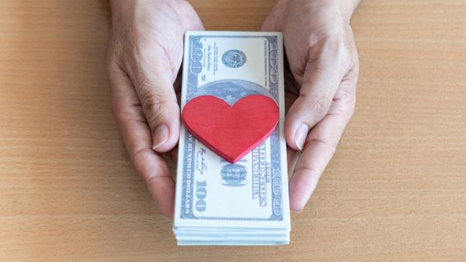 Man hands holding dollar bills and red heart on wooden table