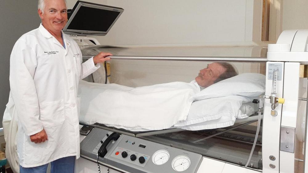 Dr. Keith Leatherbury stands near hyperbaric oxygen chamber